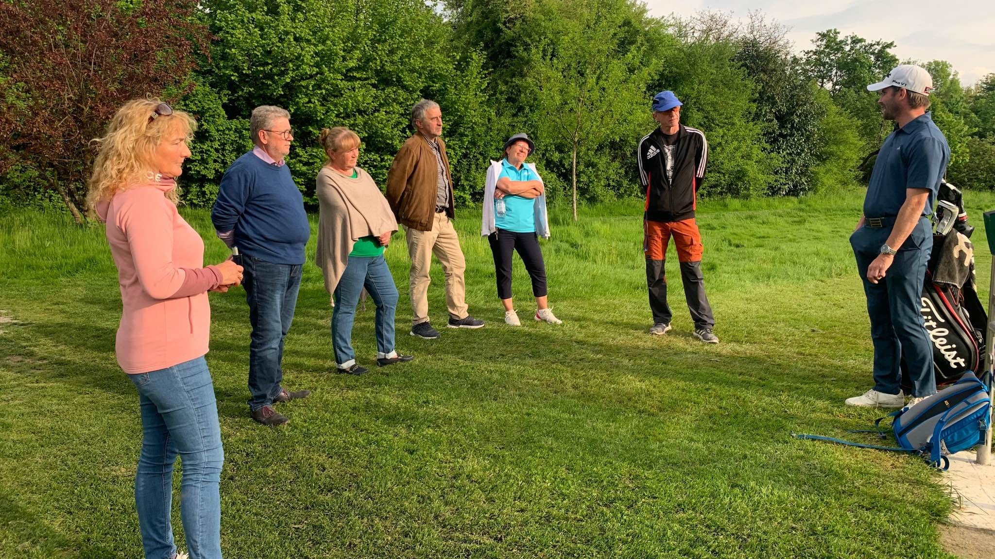 eine gruppe an menschen die einem golflehrer zuhören