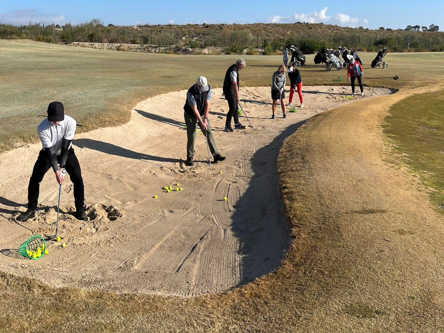 eine menschengruppe spielt golf auf einem golfplatz und schlägt dabei aus eienr sandgrube